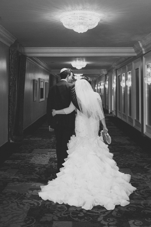 Bride and groom walk down the hall of the hotel while holding shoes in hands at end of the night