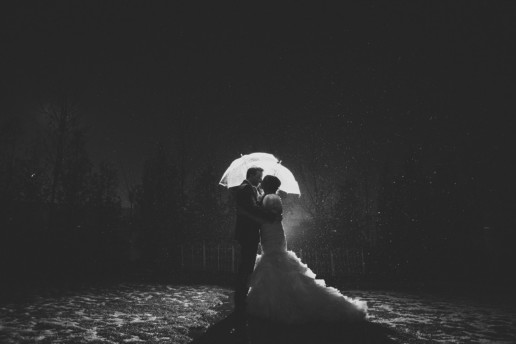 Bride and groom standing under the rain with umbrellas at night