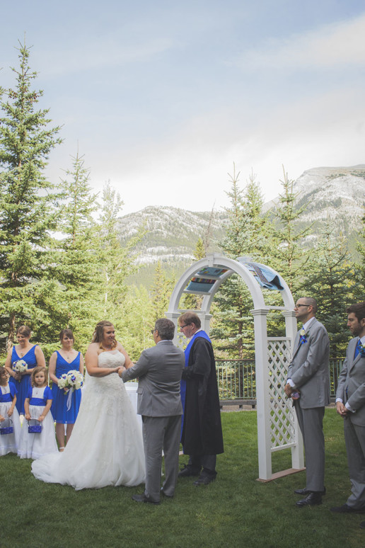 couple and bridal party stand in the shadows of the Rocky Mountains during wedding ceremony