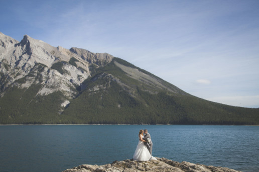 Couple stand on a rock together on their wedding day at Lake Minnewanka in Banff Alberta