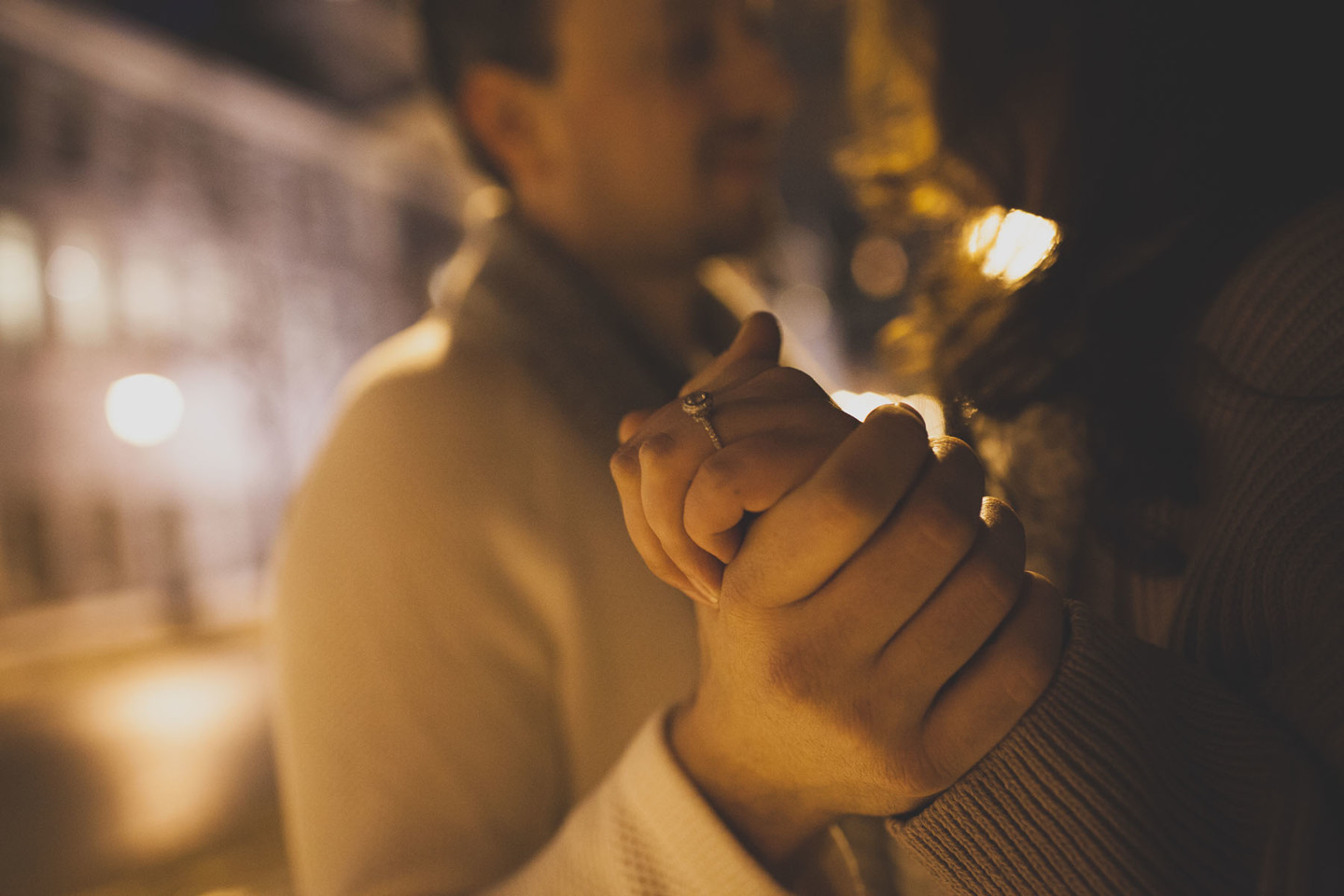 close up photo of a woman's engagement ring while a man and a woman dance under a streetlight