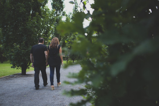 a couple are seen from behind walking together through green trees in Griffintown