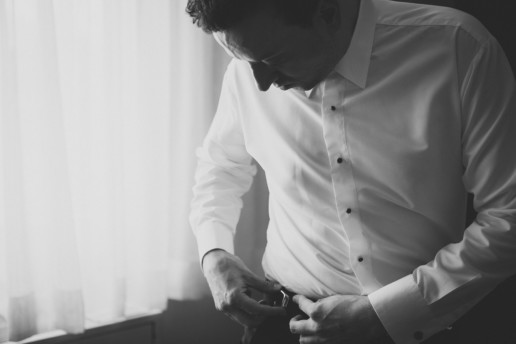 black and white photo of the groom adjusting his belt while getting dressed