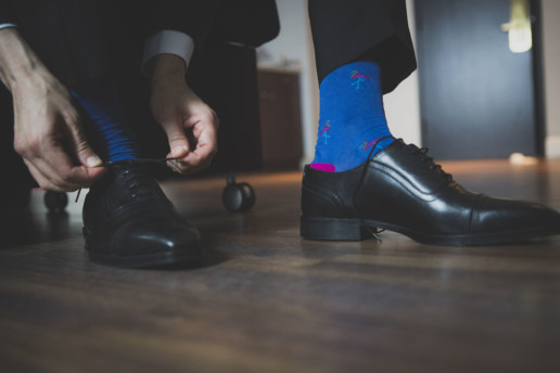 Close up of the groom putting on his shoes with fun blue socks