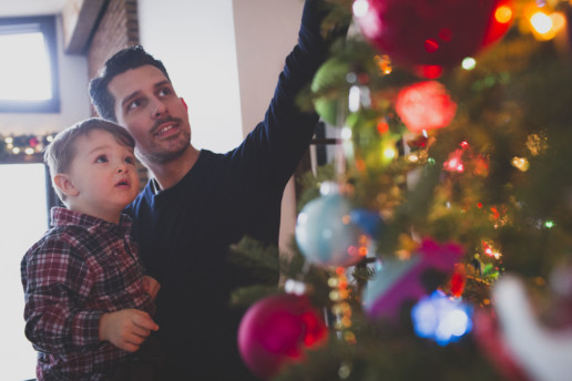 A father points out decorations on the Christmas tree to his young son in the morning