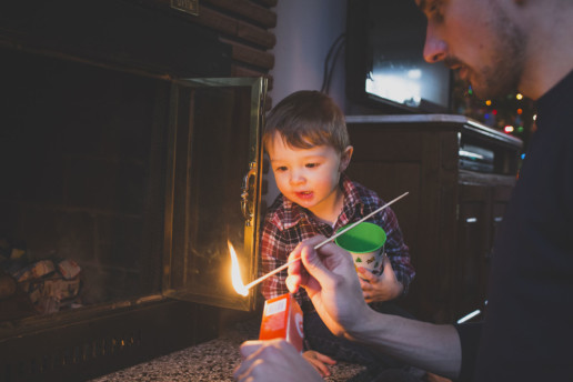 A little boy watches his father light a match to start a fire in the fireplace in Quebec