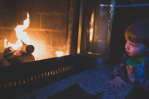 A little boy watches the flames in the fireplace of the family home in Pointe-Claire Quebec while holding his Christmas Peanuts cup