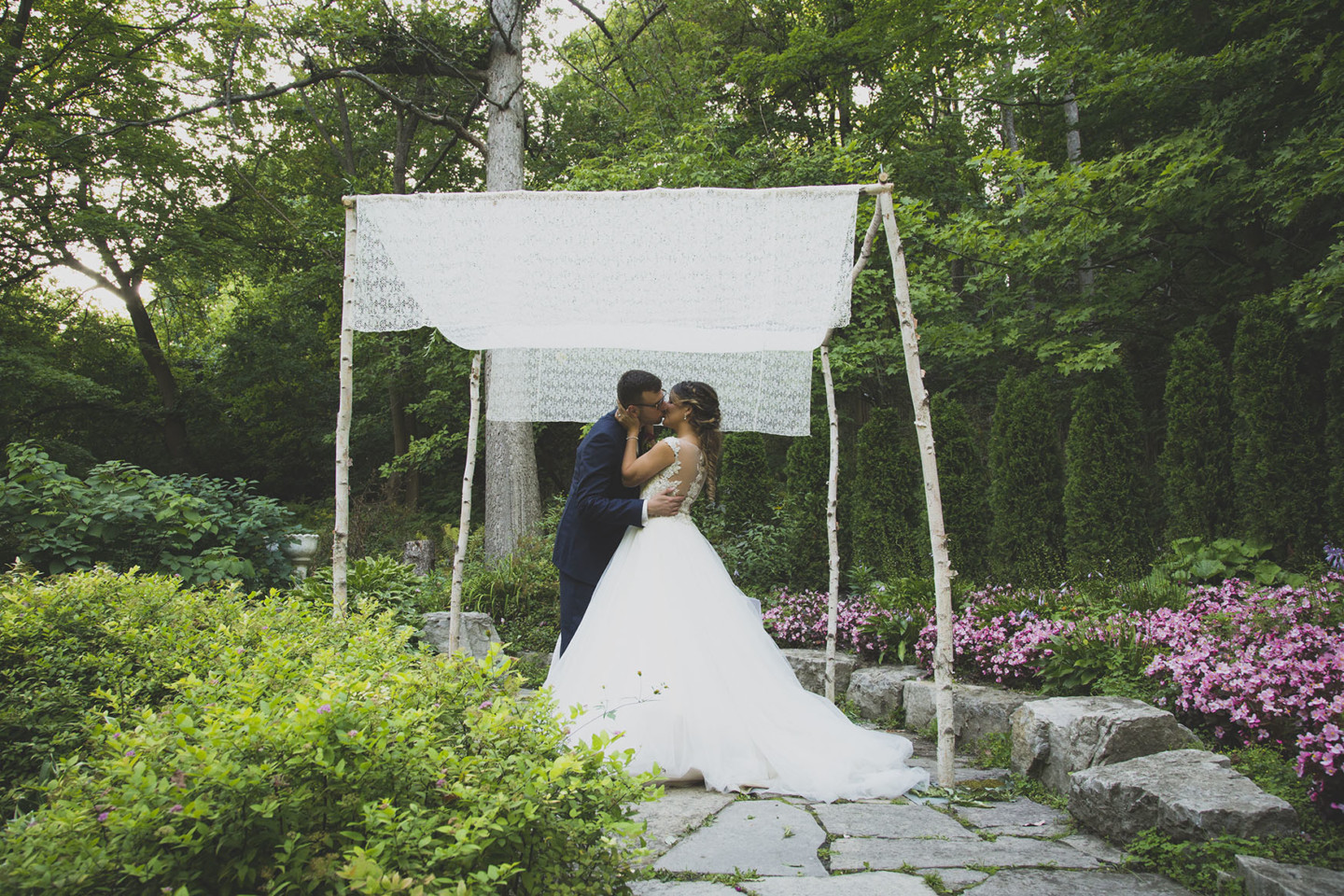 bride and groom kissing in a garden under a white lace canopy