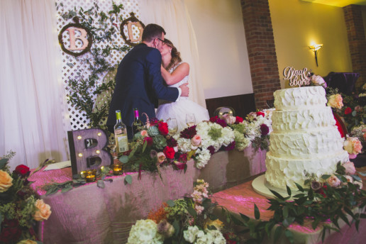 a bride and groom kiss in front of a colourful head table ladden with lots of florals in bright and bold colors