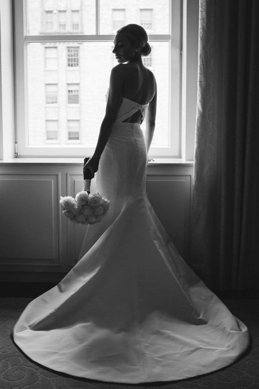 half silhouette of bride holding her bouquet of white rosese in front of window in her suite at Ritz-Carlton Montreal