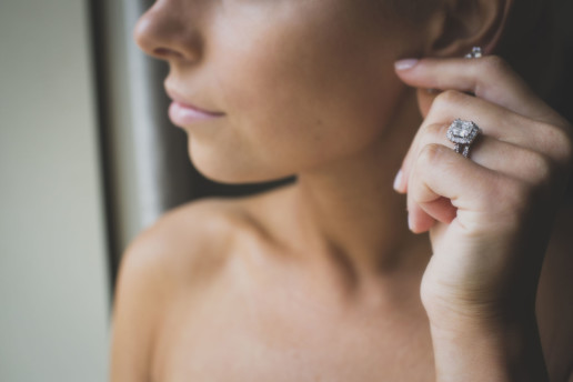 Close up of engagement ring as woman adjust her earrings by window light