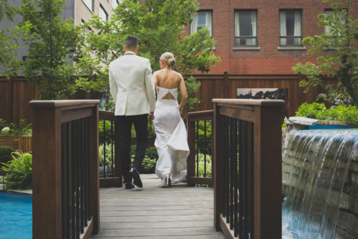 bride and groom walk on a foot bridge with a waterfall next to them in the garden of the Ritz-Carlton hotel in Montreal
