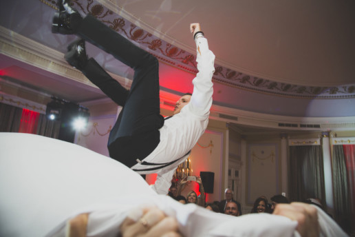 Groom is thrown in the air on a sheet during the hora dance in a Jewish wedding in the Oval room