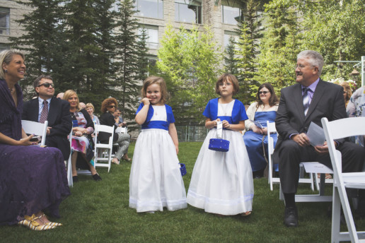 flower girls shyly walk down the aisle at outdorr wedding ceremony at the Rimrock Resort hotel in Banff