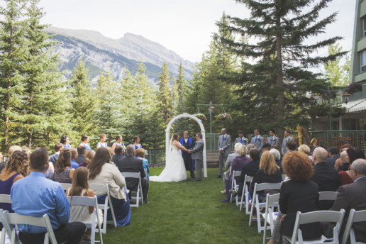 couple hold hands with their bridal party and guests all around outside at the Rimrock Resort and hotel in Banff