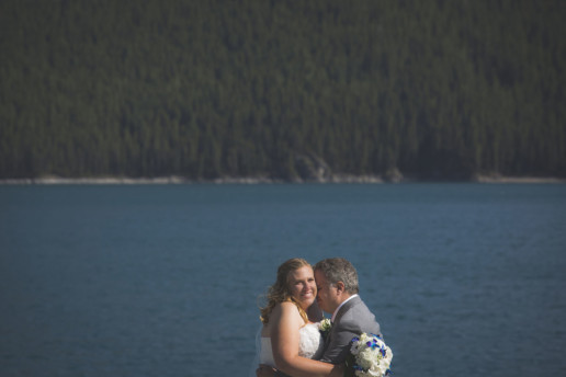 Bride smiles while being held by her groom at Lake Minnewanka in Banff Alberta