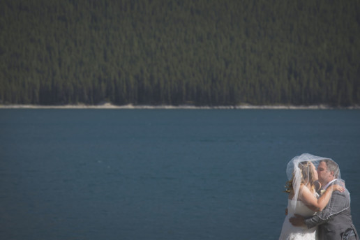 couple kissing under the wedding veil in front of lake Minnewanka in Banff Alberta