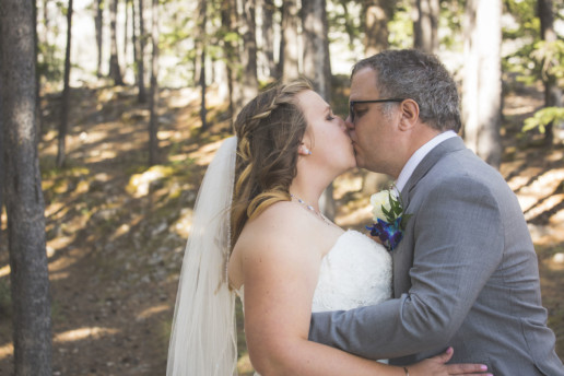 bride and groom kiss in the sunner forest juts off Lake Minnewanka in Alberta