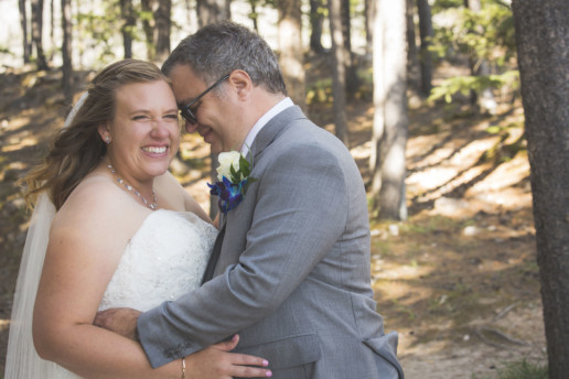 Bride laughs while being held by the groom in the sunny forest in Alberta
