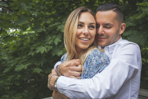 a man and woman have their engagement photo while embracing in front of lush green trees