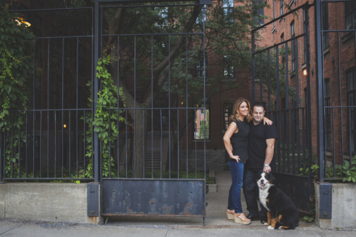 a man and woman hold their dog for their engagement photo in griffintown